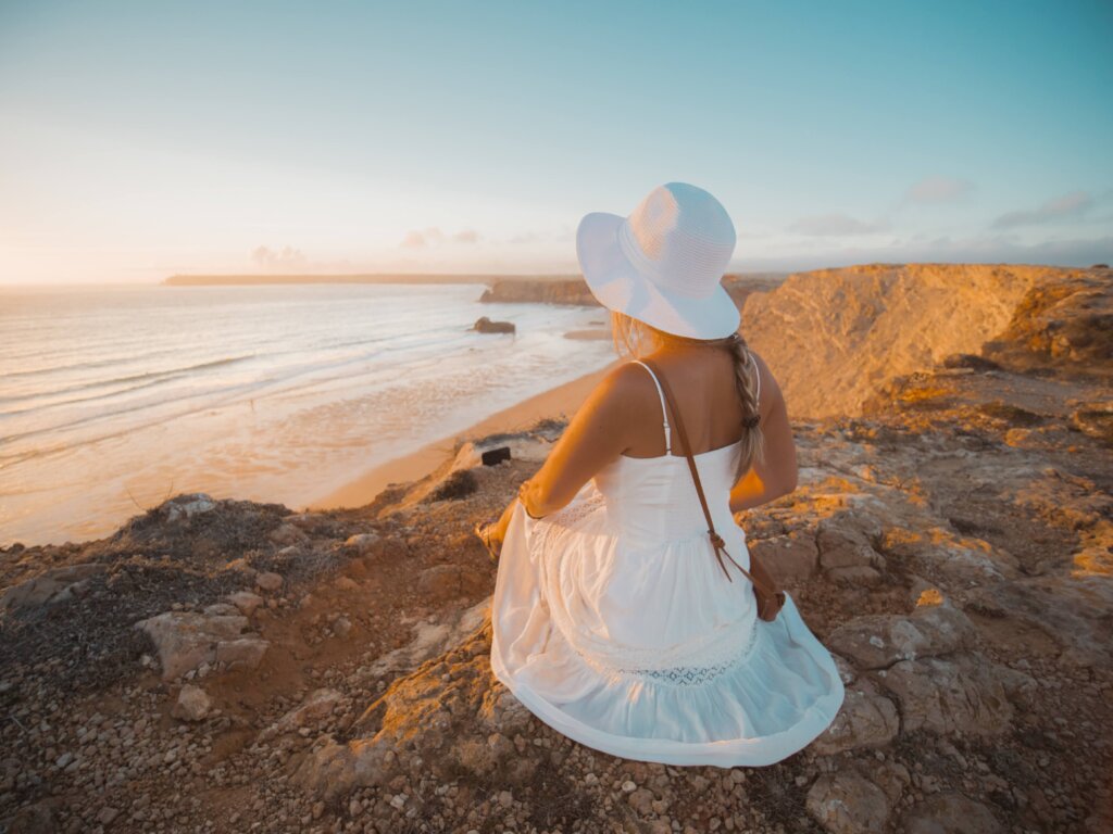 Image of a woman sitting on a cliff during sunset at Praia do Tonel, one of the best things to do in Portugal.